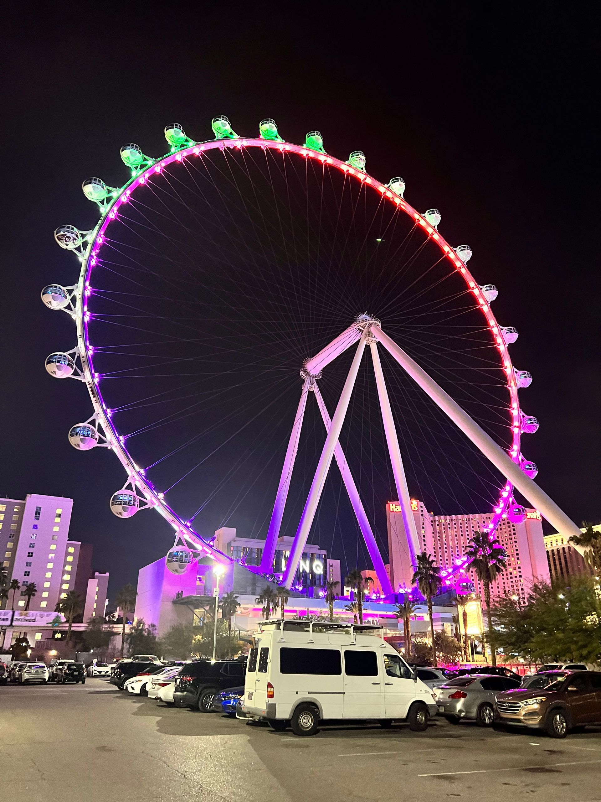 Giant Ferris wheel at night with colorful lights in Las Vegas. Cars parked in front.