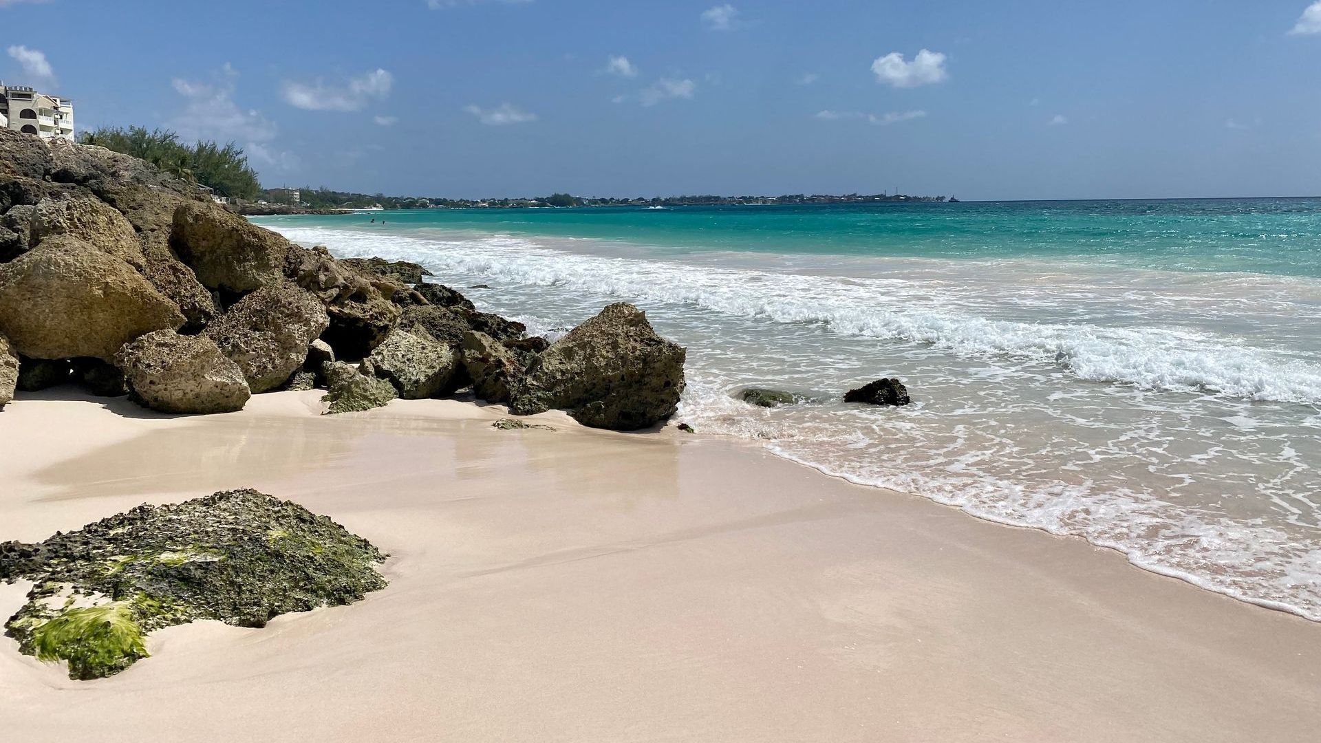 Sandy beach in Barbados with rocks, turquoise water, and blue sky.