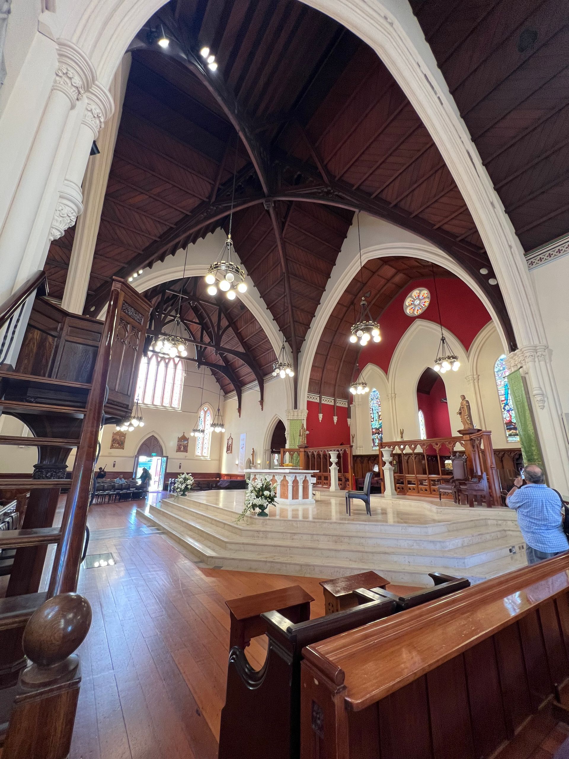 Inside of a church with wooden arches, white walls, red accents, and pews.