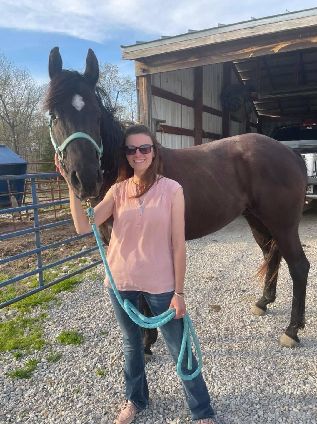 A woman is standing next to a black horse on a leash.