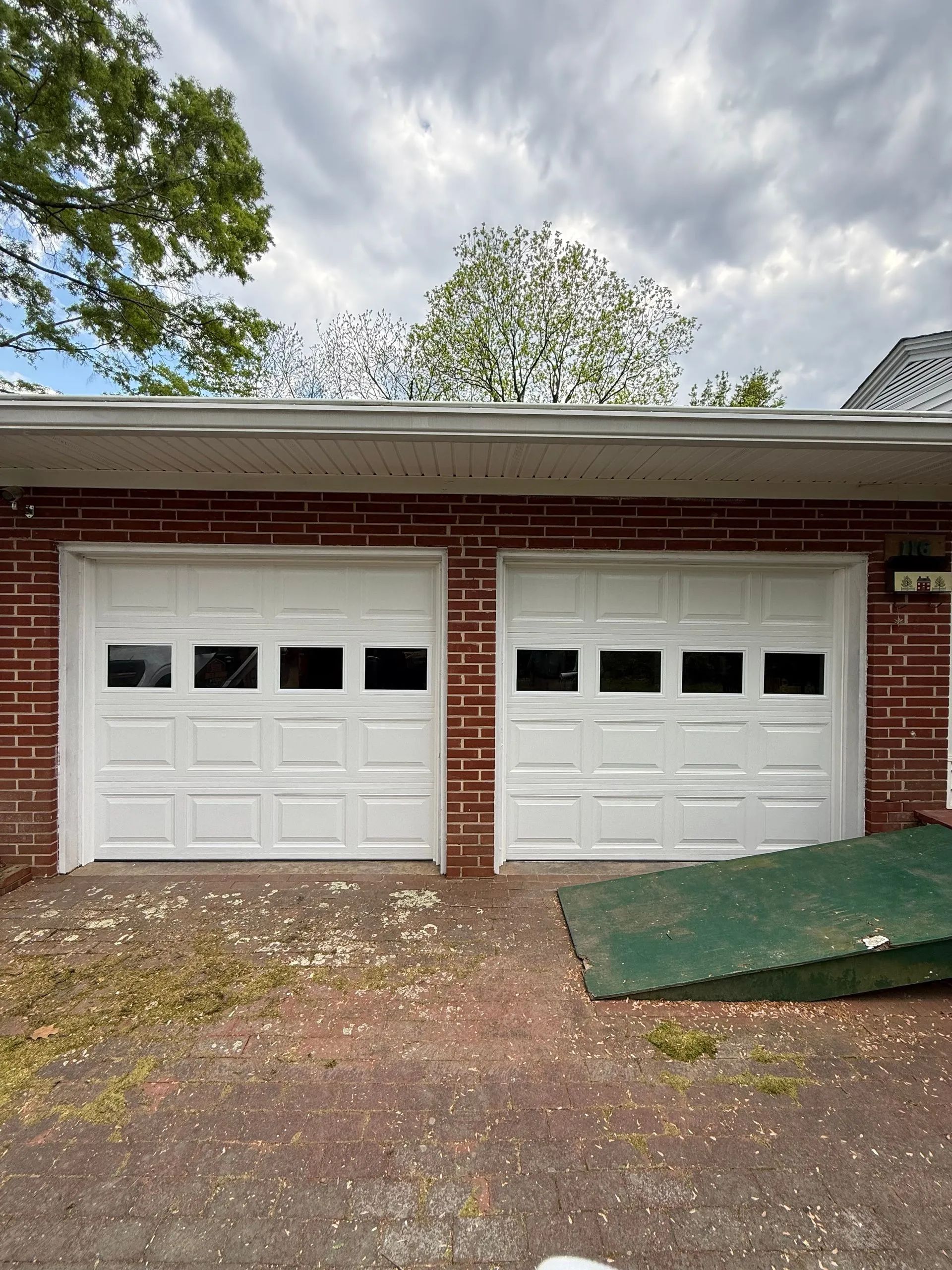 Brick garage with two white doors and a green ramp on the right under cloudy skies
