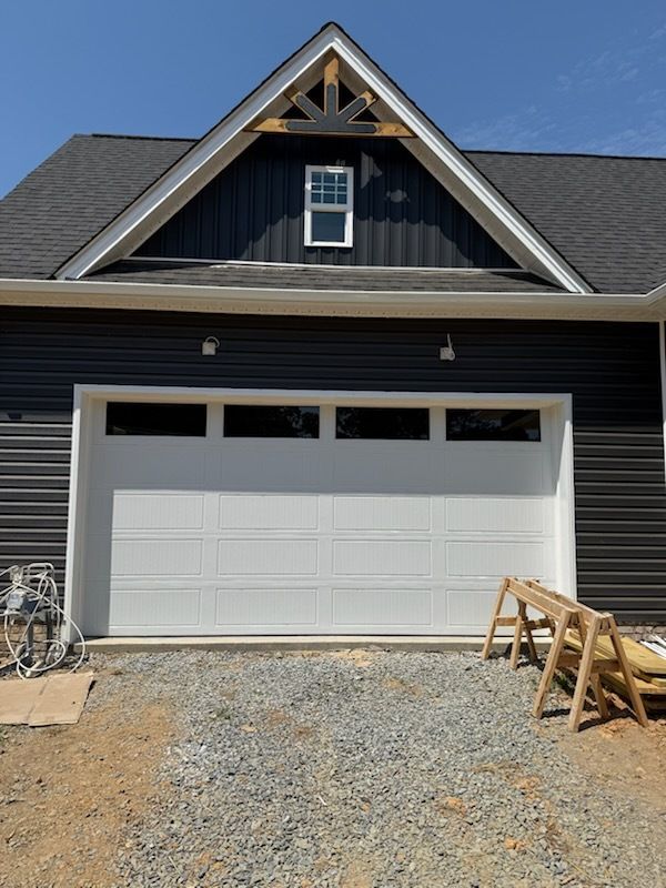 New house with a white garage door, black siding, and construction materials in the driveway.