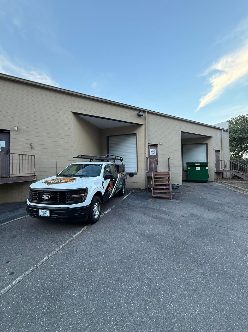 Pickup truck parked outside a beige warehouse with loading docks and a green dumpster