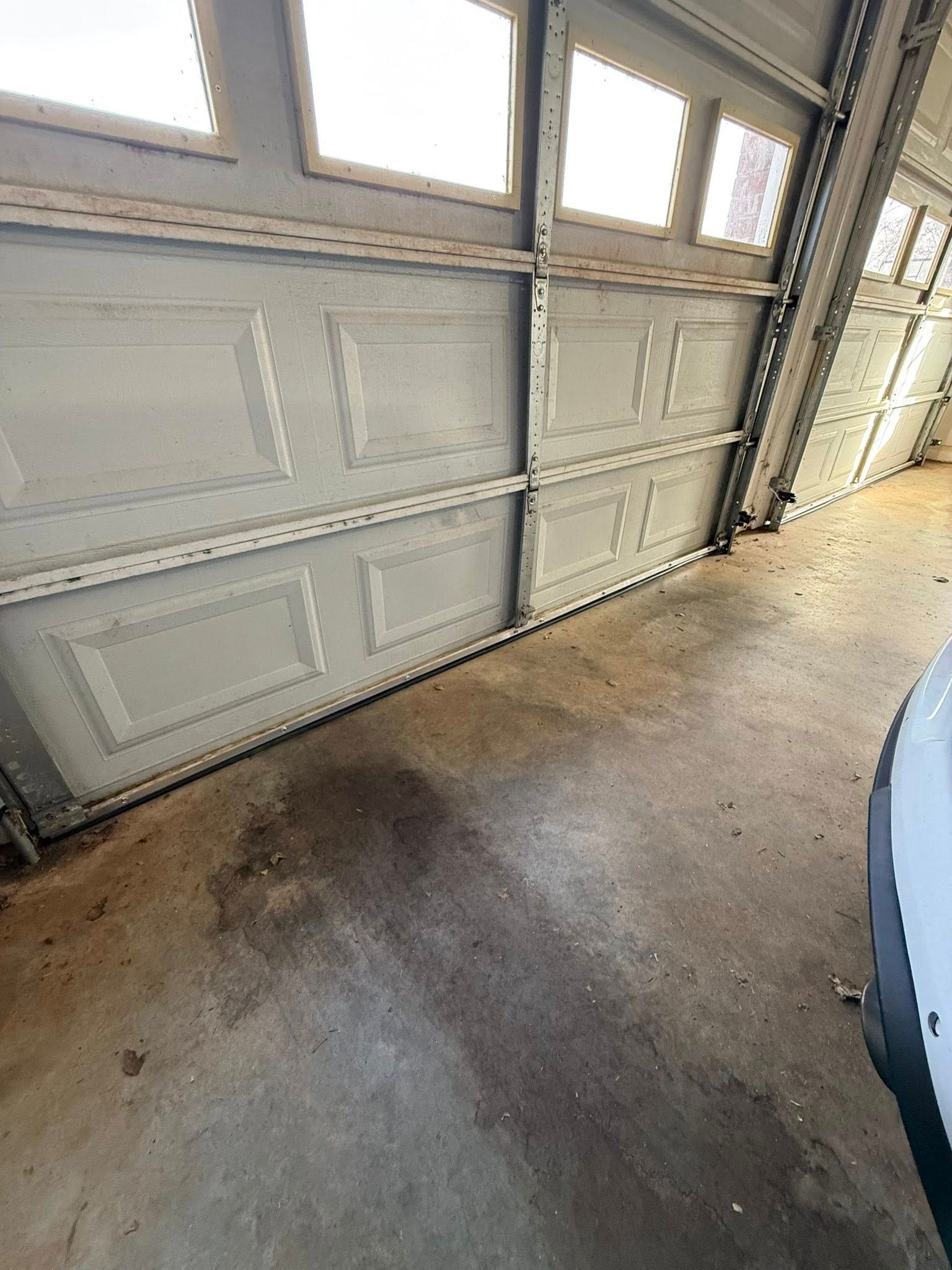 Interior view of a garage door and concrete floor with sunlight coming through windows.