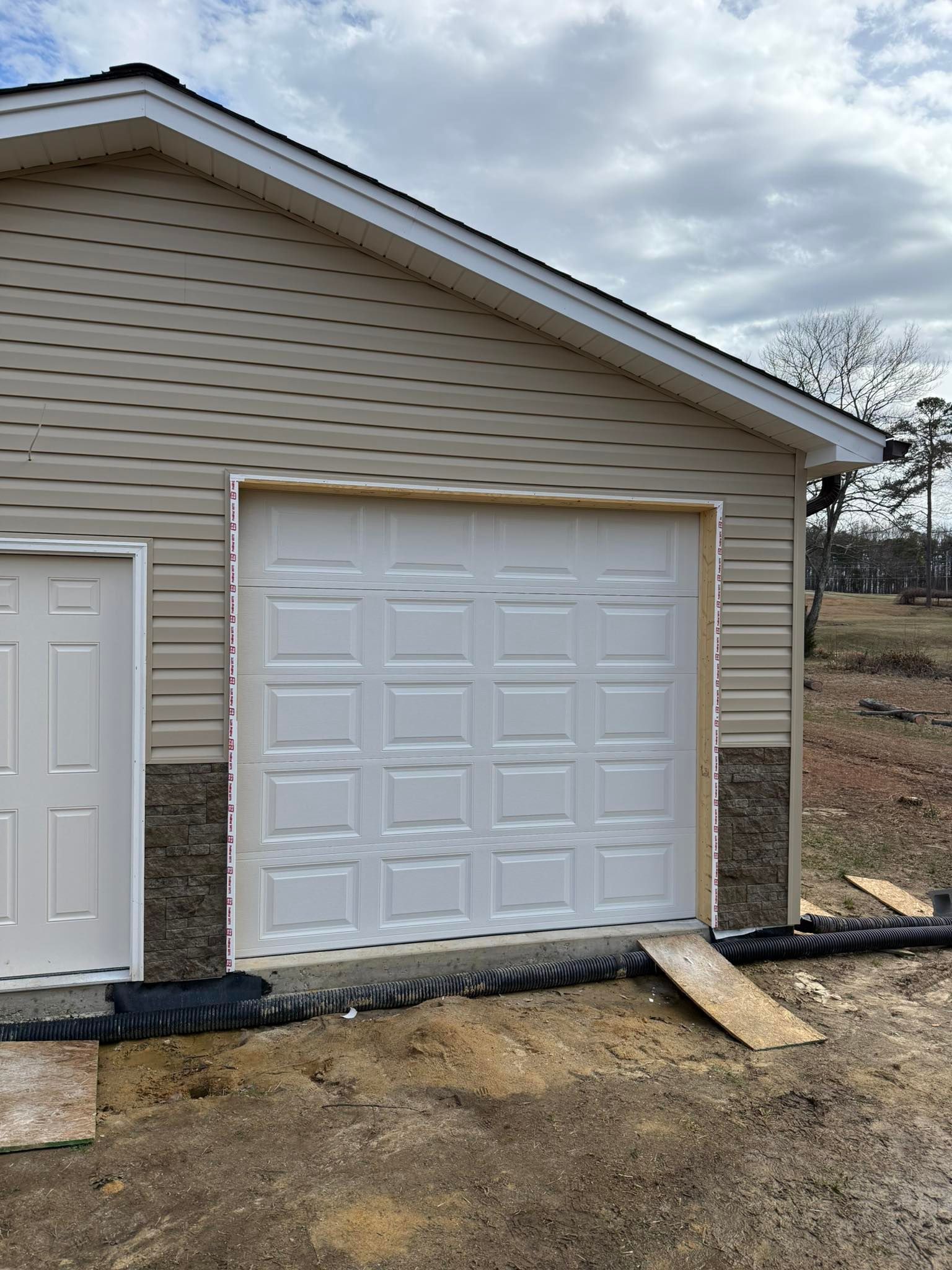 White garage door on beige detached garage with a ramp in front, under cloudy sky.