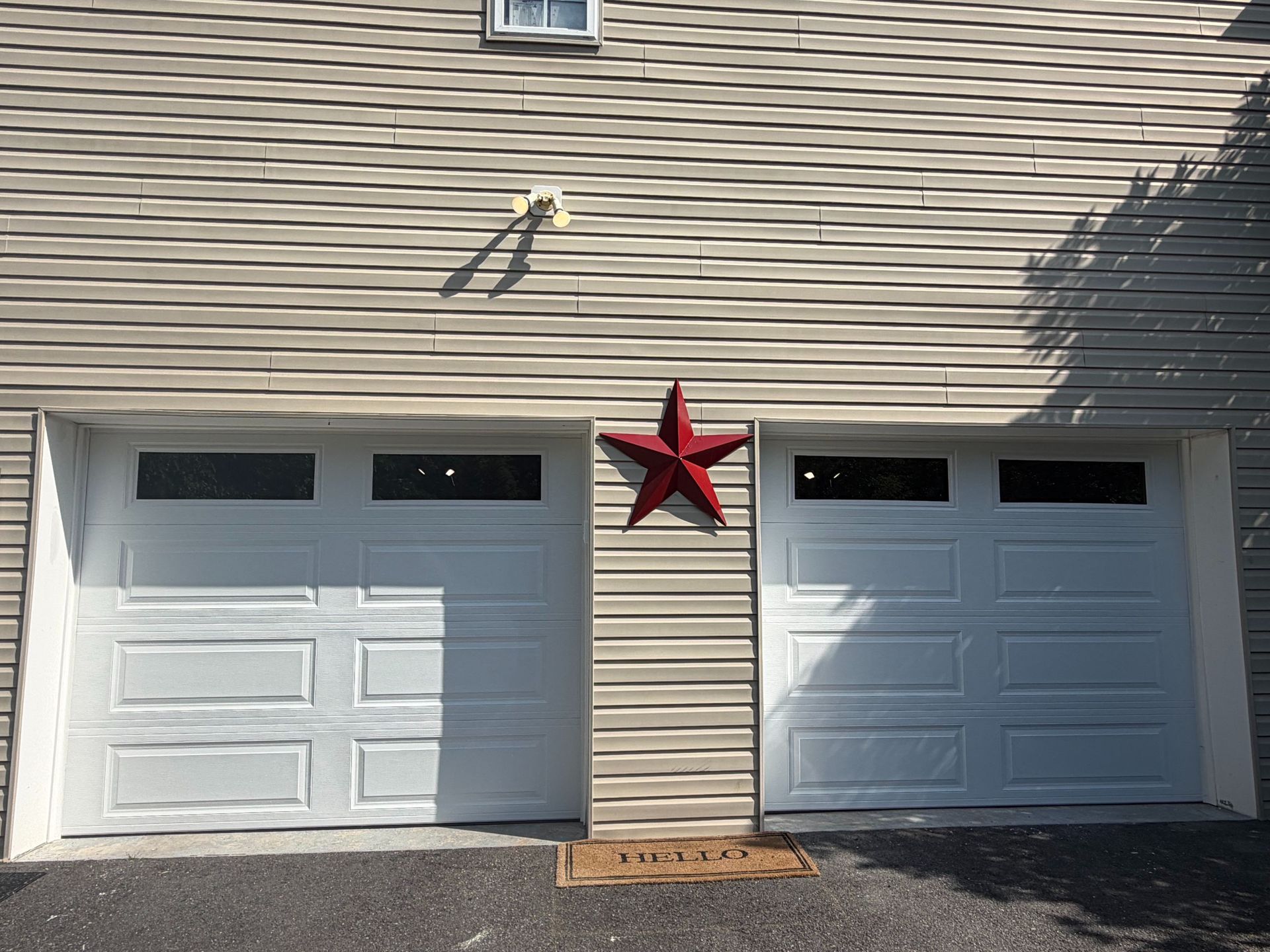 Two white garage doors under a dark shingled roof on a concrete driveway