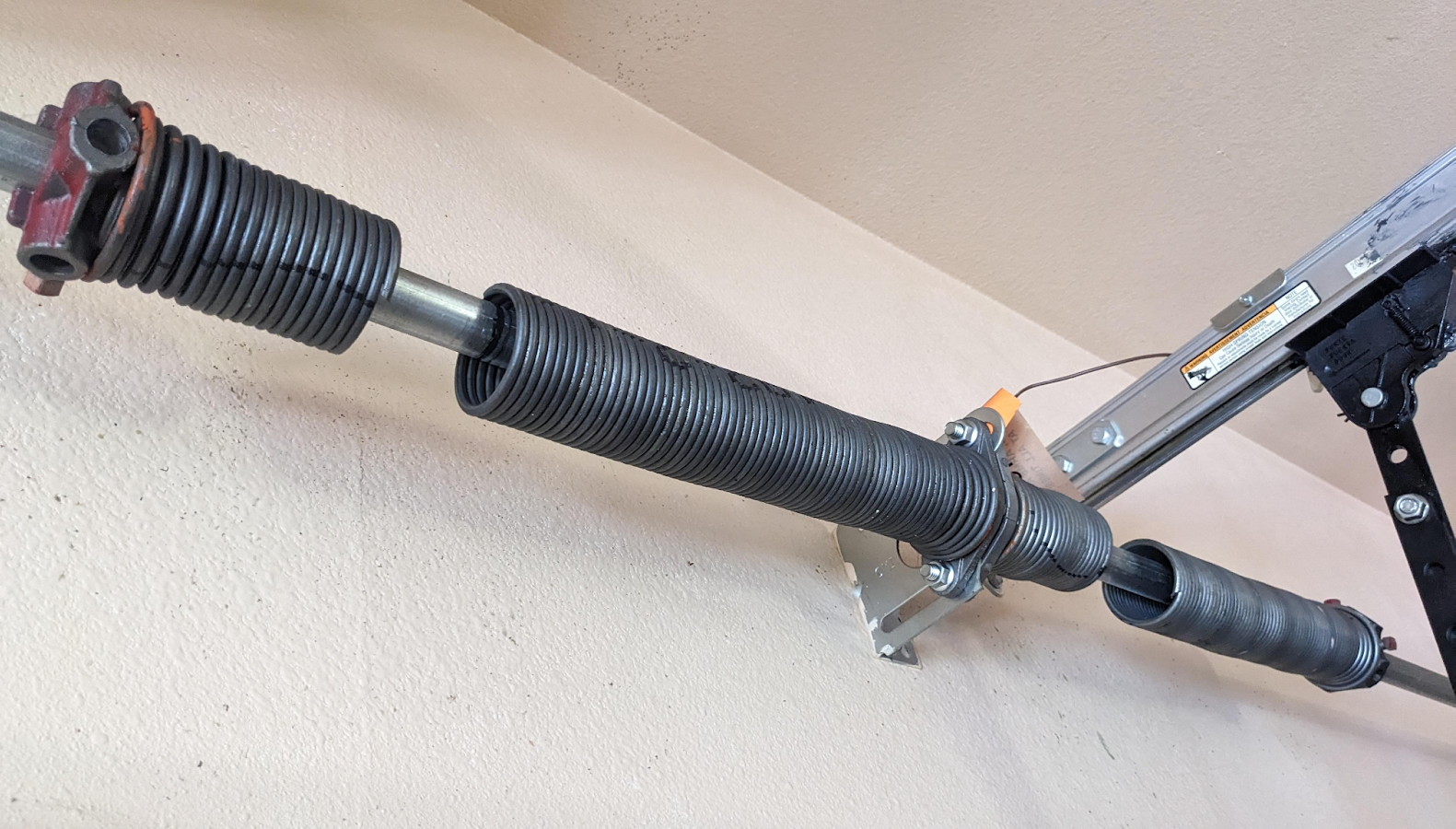 Black garage door torsion spring assembly mounted above a door, with a winding bar attached.