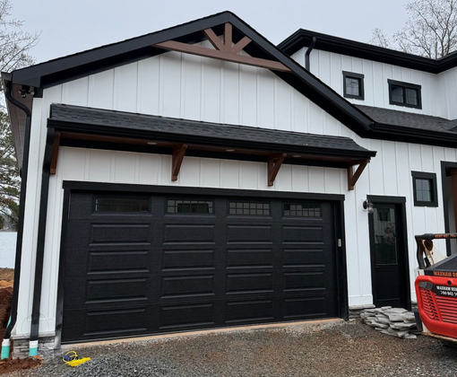 Two white garage doors beneath a dark shingled roof on a concrete driveway