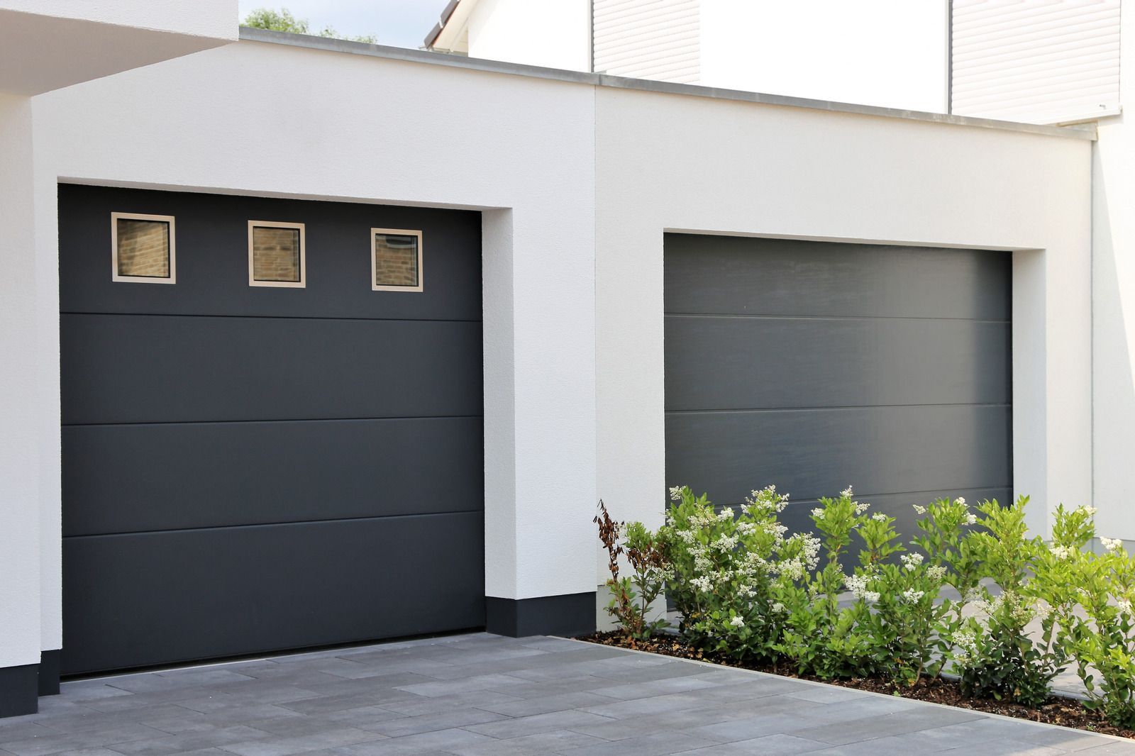 Modern white house exterior with two dark garage doors and shrubs in front
