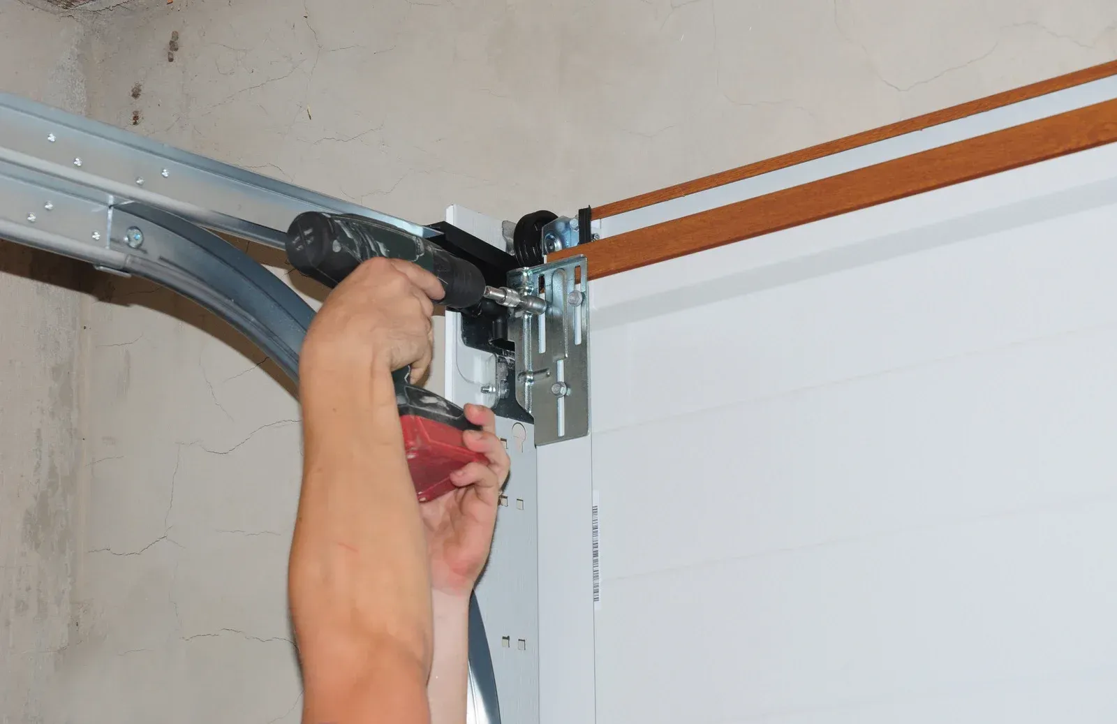 Person using a red power drill to install a garage door opener on a metal track
