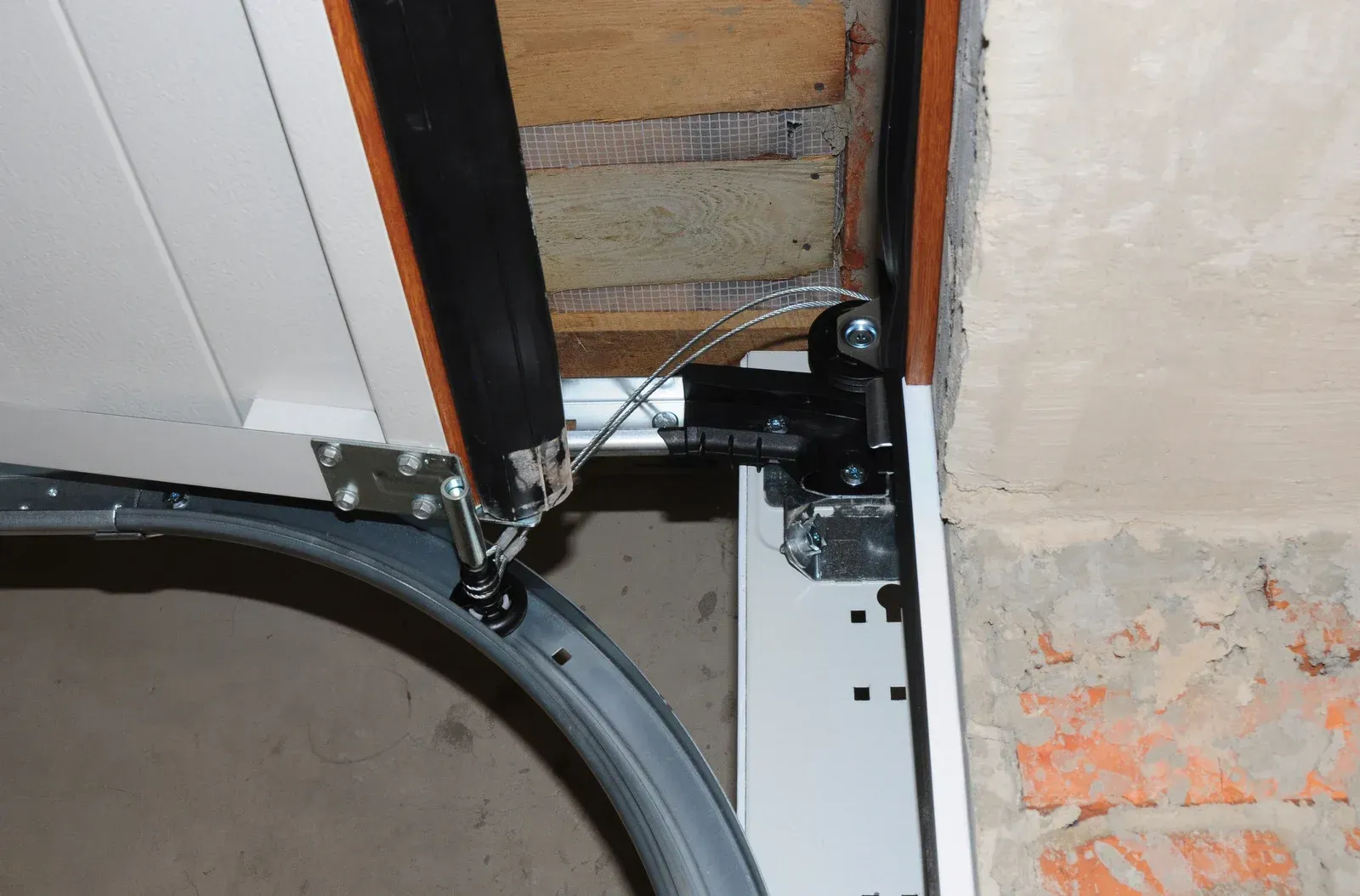 Close-up of a garage door corner with black hardware, white paneling, and a damaged wall edge.