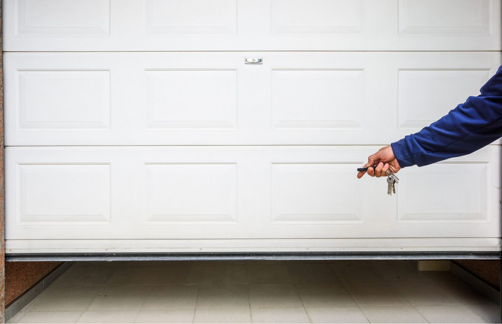 Person in blue jacket holding garage door opener toward closed white garage door