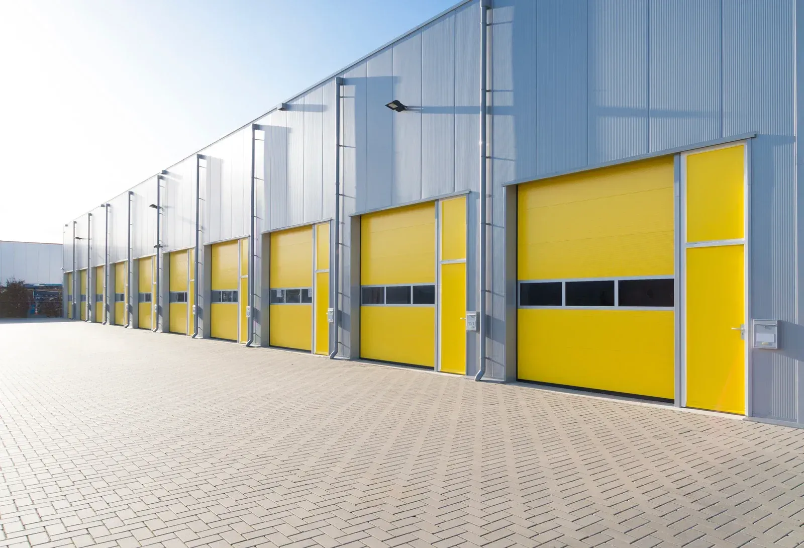Row of modern industrial warehouse units with bright yellow loading doors and gray metal siding