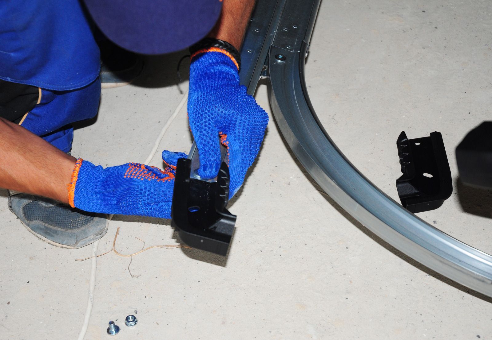 Blue-gloved hands install a black fitting on a curved gray tube on the floor