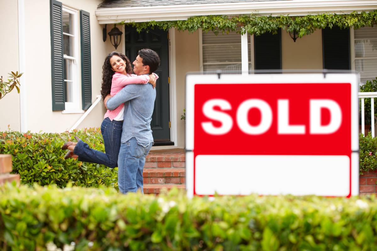 A young couple hugs behind a SOLD sign next to a house near Lexington, Kentucky (KY)