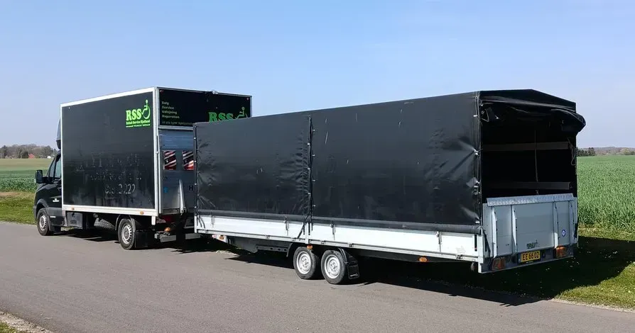 Sort lastbil trækker en sort trailer på en vej ved siden af en mark under en blå himmel.