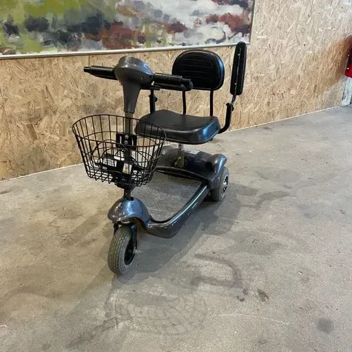 Mørkegrå mobilitetsscooter med kurv, sort sæde og ryglæn på et betongulv.
