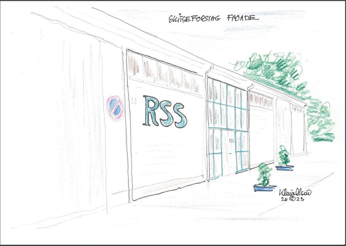 Mand med briller sidder ved et skrivebord iført en sort skjorte. Kontormiljø med papirer og en computer.