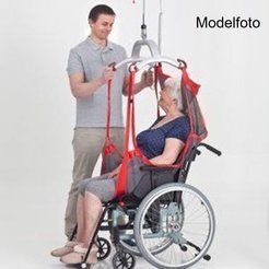 Person, der hjælper en anden ind i en kørestol ved hjælp af en rød slynge og loftlift. Indendørs, hvid baggrund.