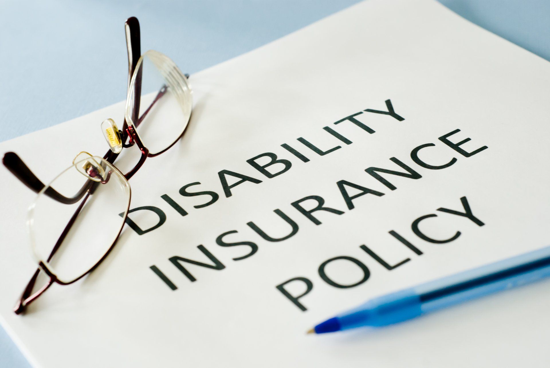 Disability Insurance Policy document with glasses and pen