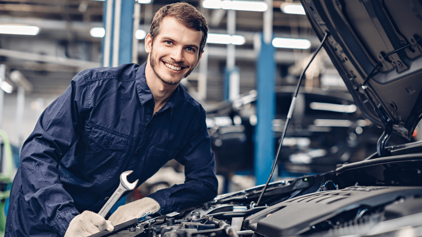 smiling mechanics holding a wrench under hood of a car