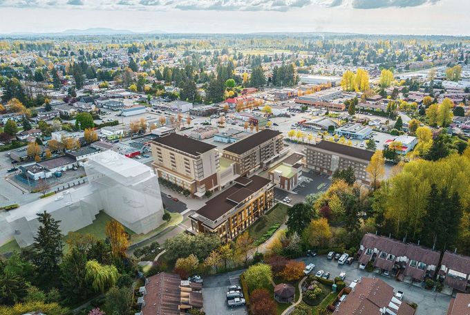 Aerial view of a suburban campus with buildings, parking lots, trees, and a distant city skyline