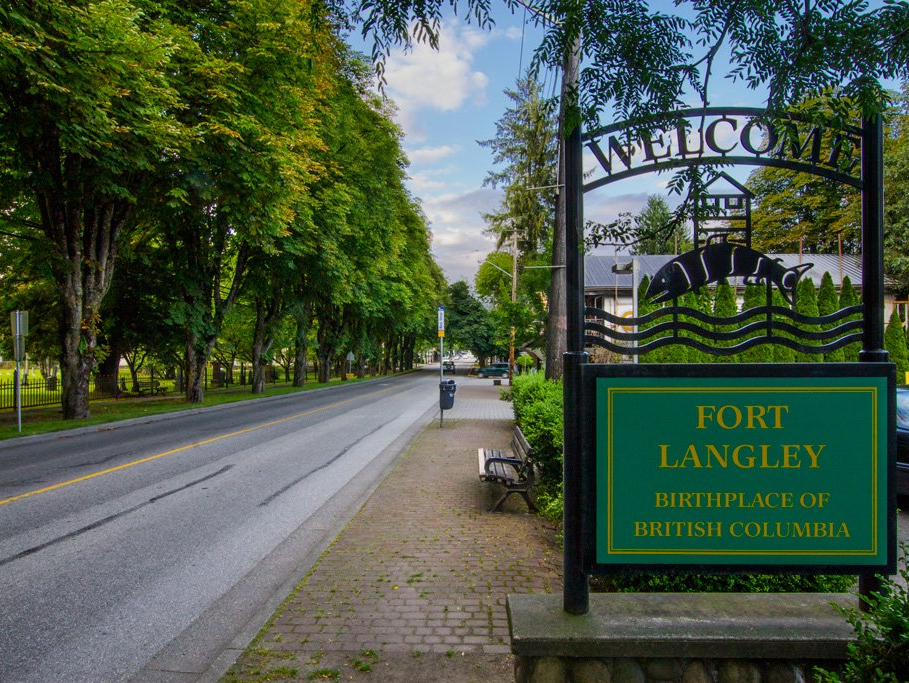 Fort Langley village entrance sign beside a tree-lined road on a rainy day