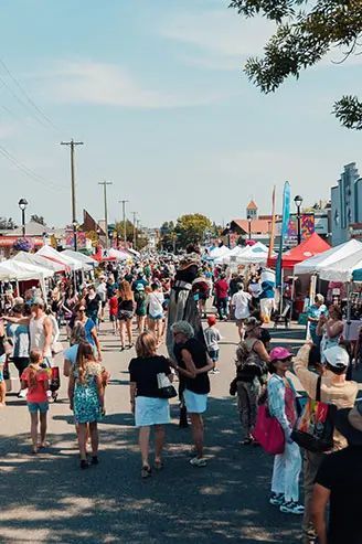 Crowded outdoor street market with tents, pedestrians, and city buildings in the background