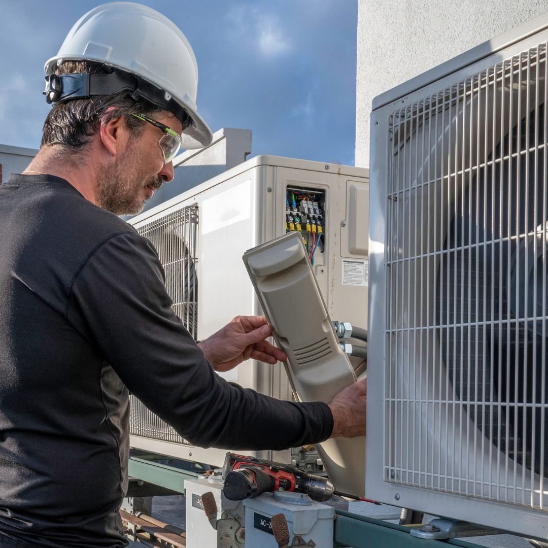 A man wearing a hard hat is working on an air conditioner.