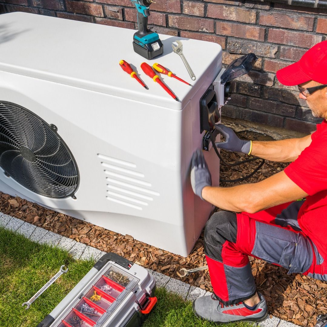 A man in a red hat is working on an air conditioner.