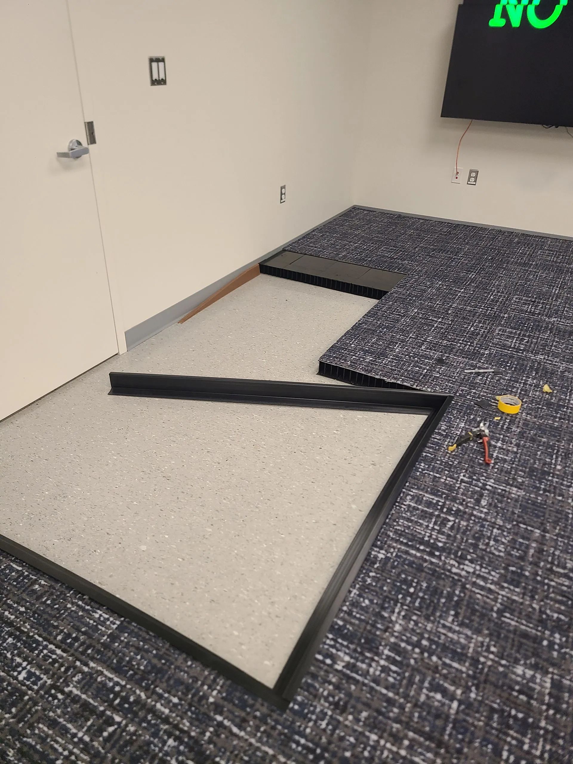 Room with carpeted floor, sections of exposed concrete, and black border trim.