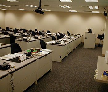 Rows of desks in a beige-walled room, possibly a classroom or conference room.