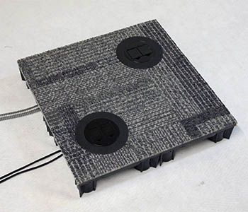 Gray carpeted floor tile with two black pop-up electrical outlets and connected wires.