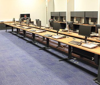 Computer lab with long desks, monitors, and keyboards on blue carpet.