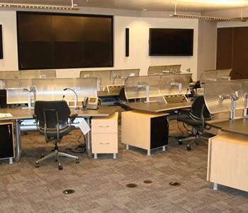 Office with several desks, large screens, and sound baffles. Beige, black, and silver color scheme.