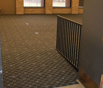 Interior view of empty room with checkered carpet, windows, and black metal railing.