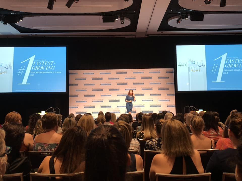 A woman is giving a speech in front of a crowd at a conference