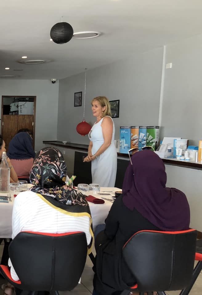 A woman is standing in front of a group of people sitting at tables.