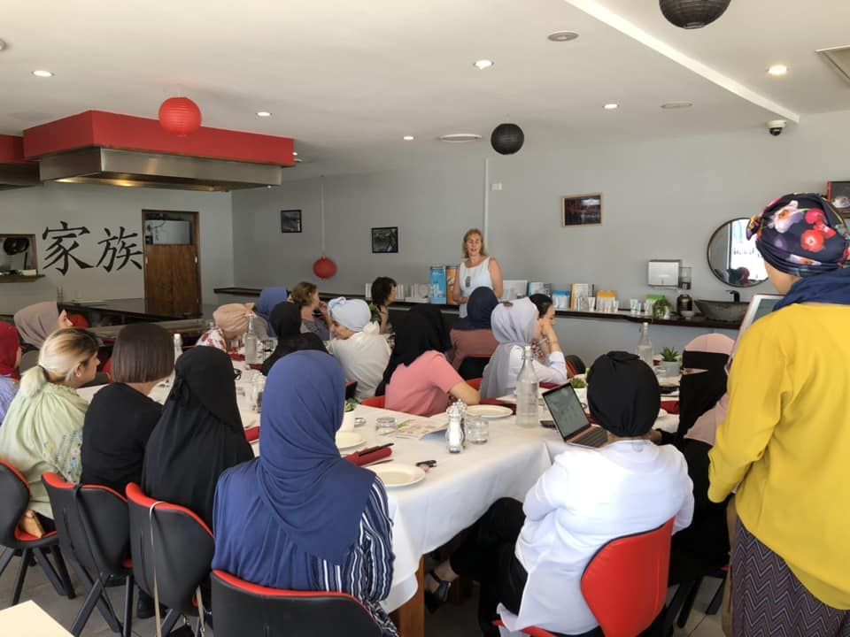 A woman is giving a presentation to a group of people sitting at tables.