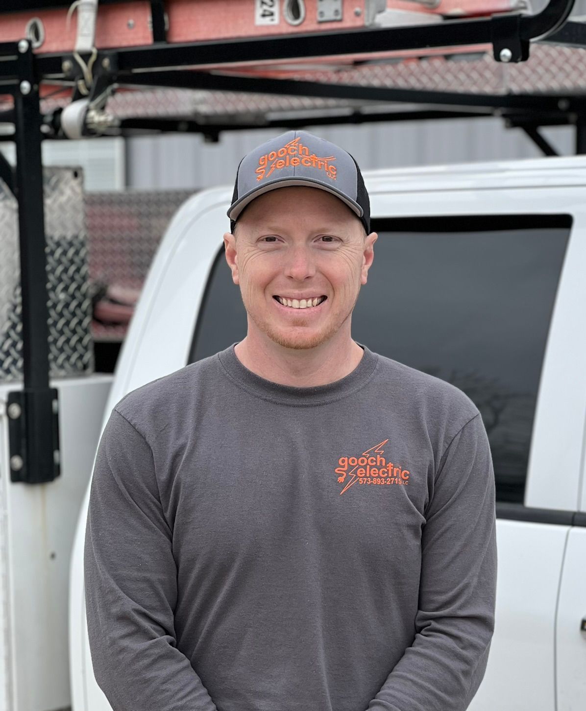 Chris Gooch wearing a hat and a gray shirt is standing in front of a white truck.