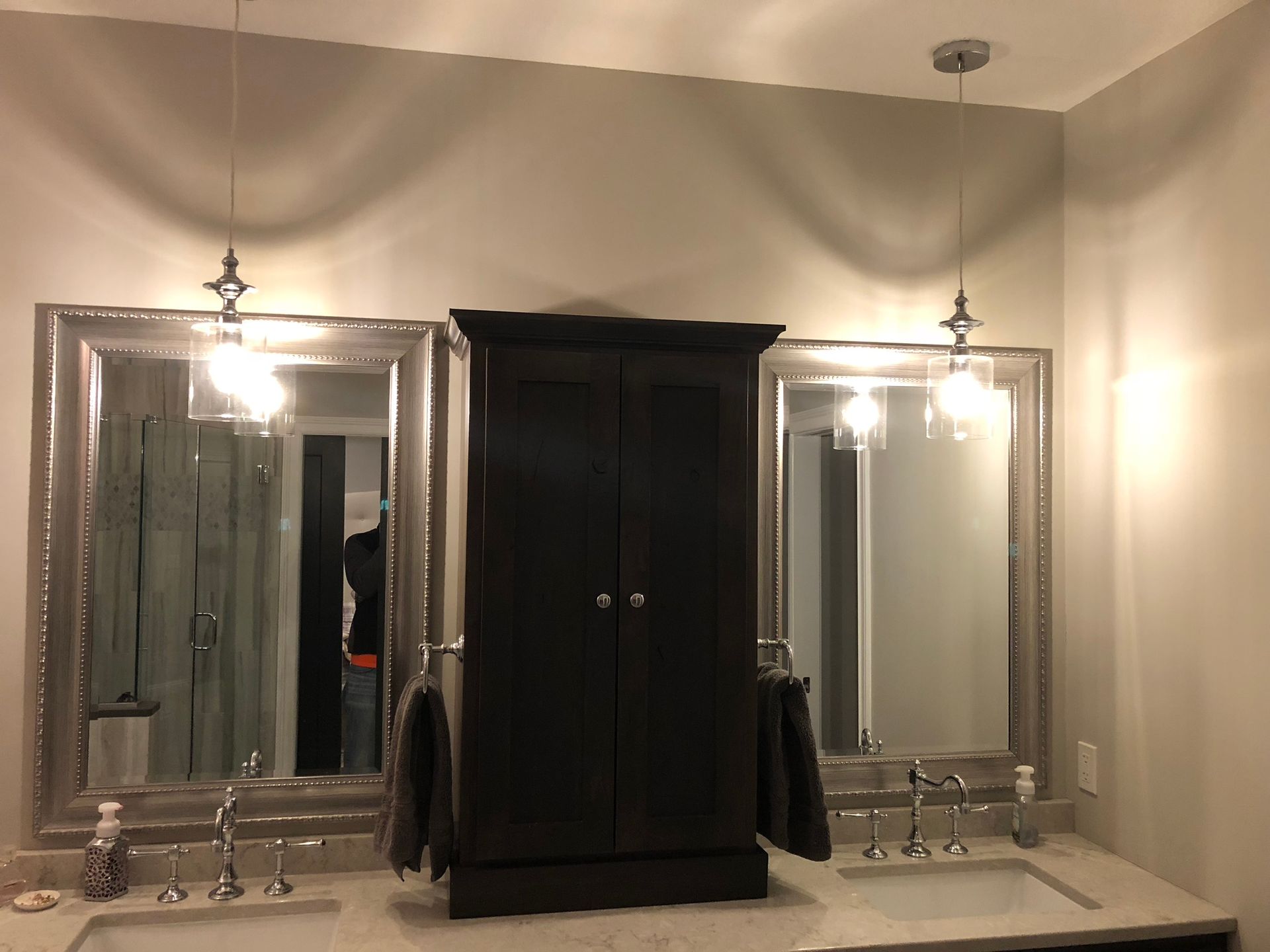A bathroom with two sinks , two mirrors and a cabinet.