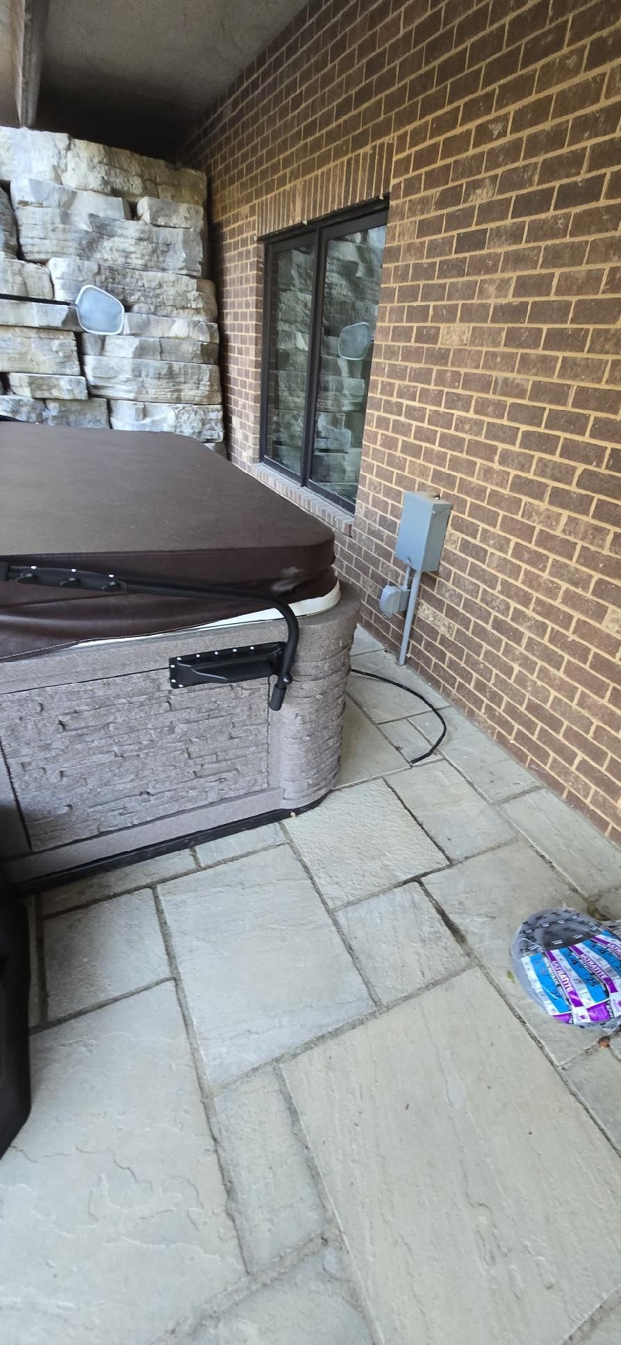 A hot tub is sitting on a patio in front of a brick building.