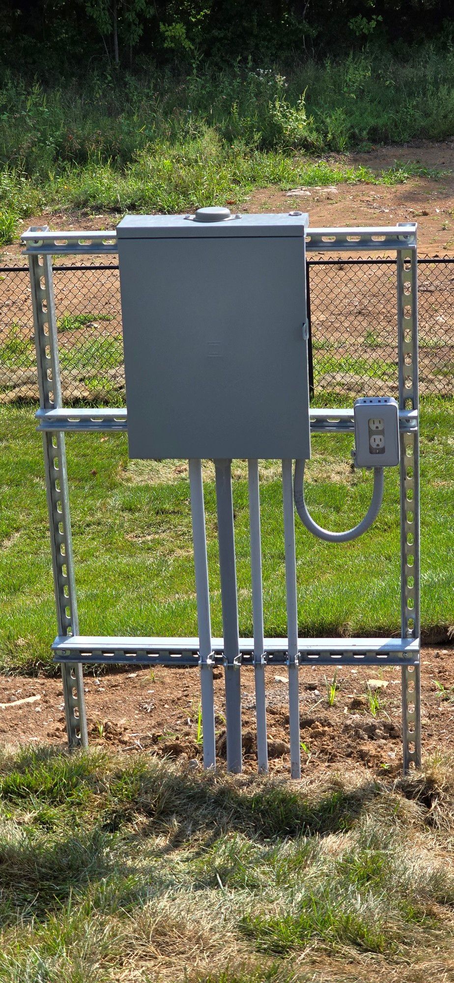 A box is sitting on top of a metal pole in the grass.