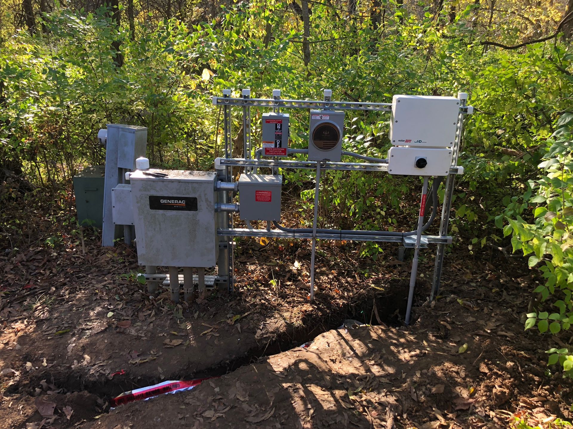 A bunch of electrical boxes are sitting in the dirt in the woods.