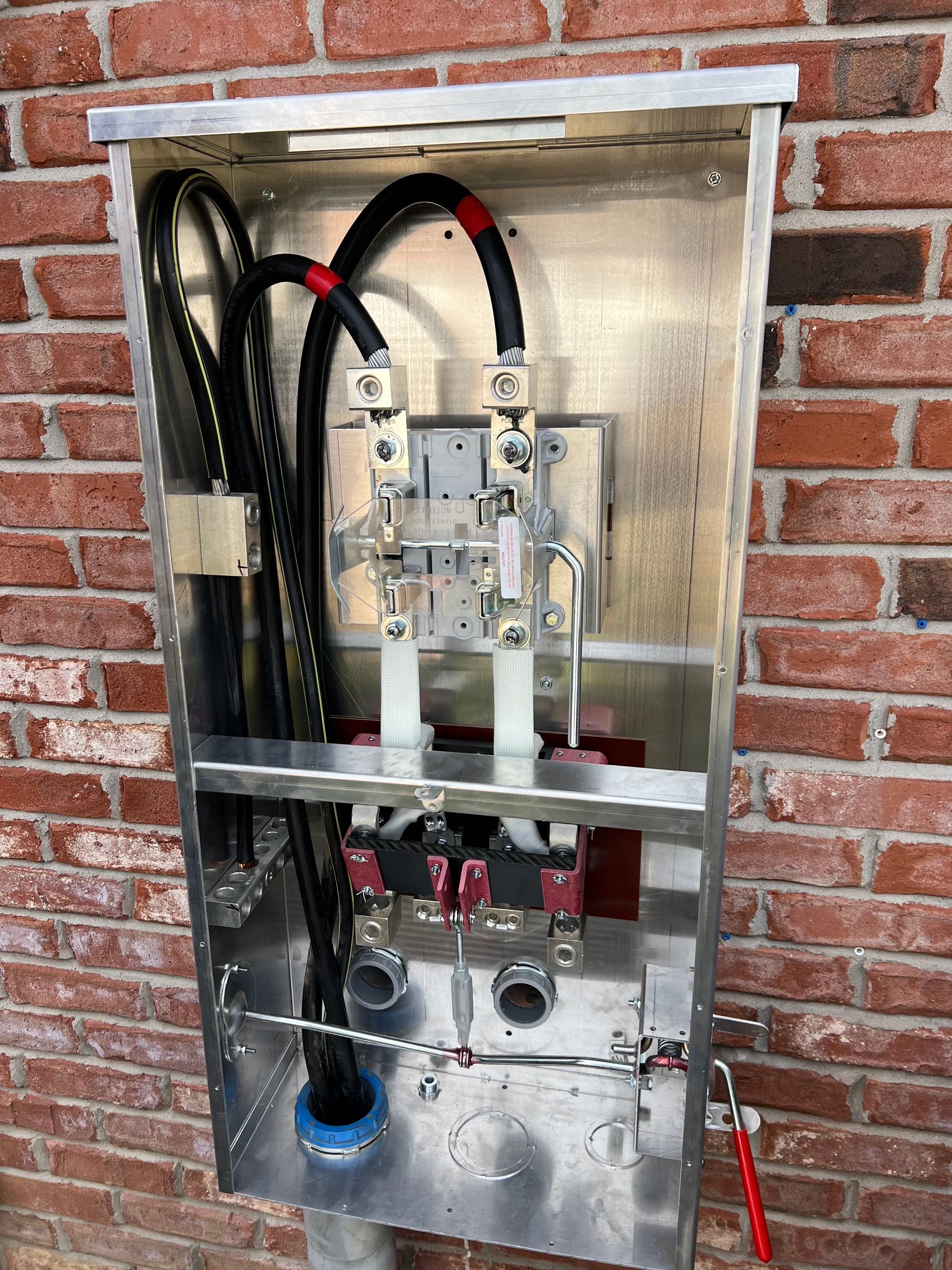 An electrical box is sitting on a brick wall.