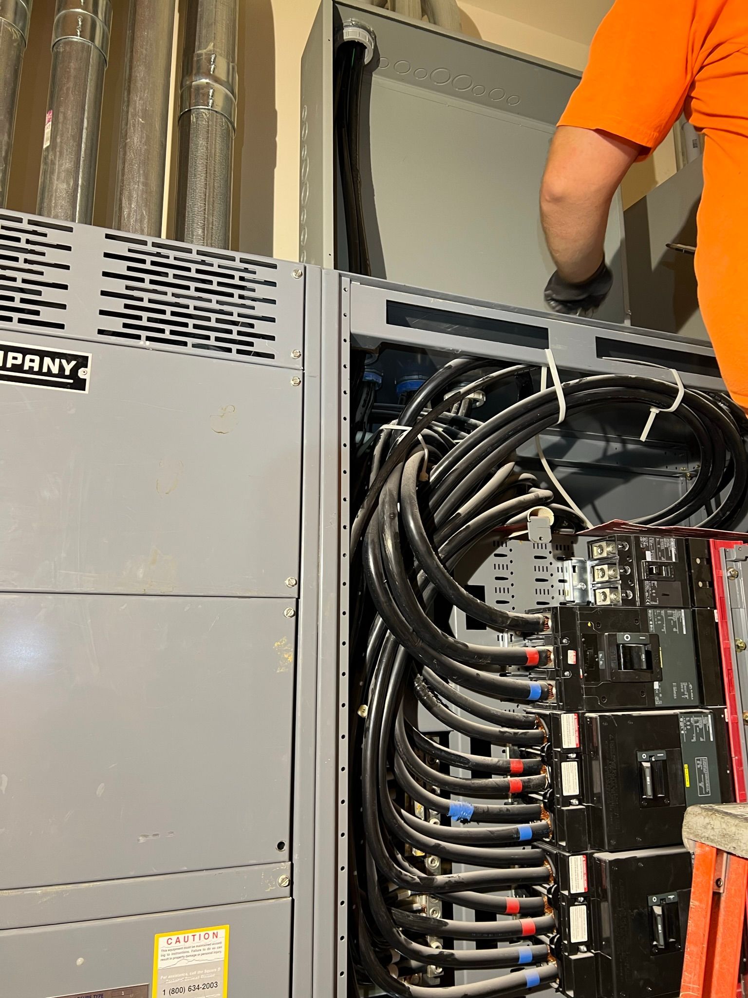 A man in an orange shirt is working on an electrical box.