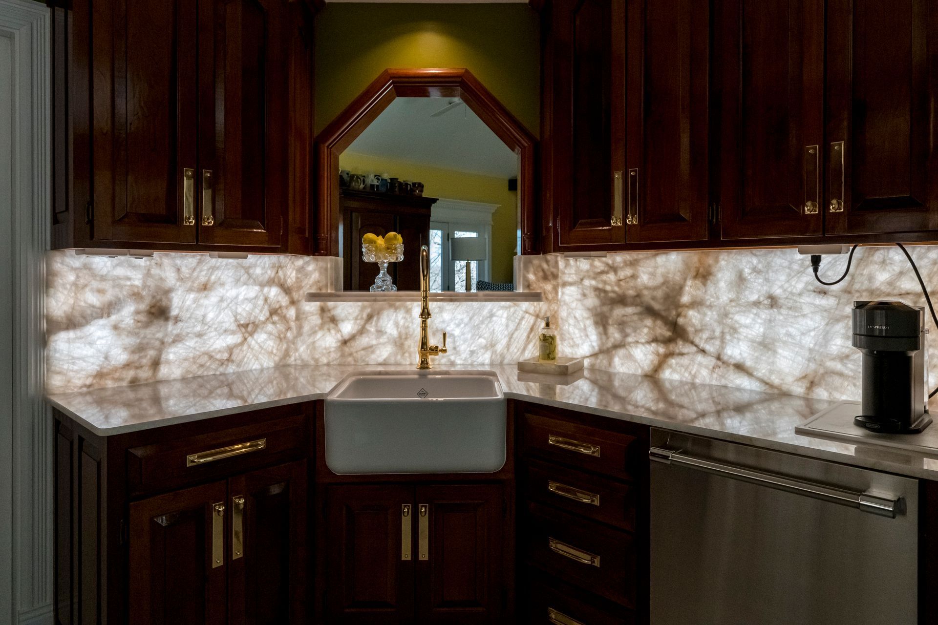 Kitchen with dark wood cabinets, backlit stone backsplash, white sink, and stainless steel appliances.