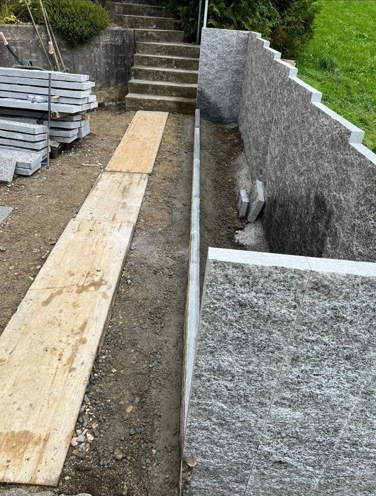 Neben einer Steinmauer wird ein Holzsteg gebaut.