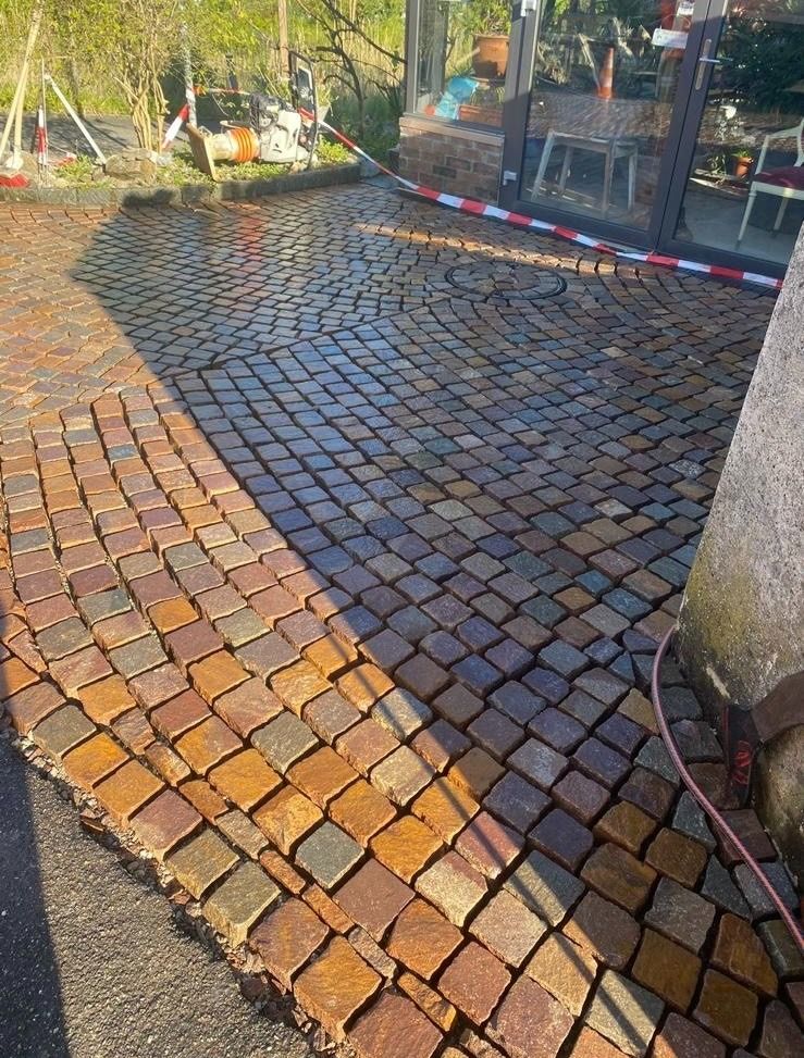 Ein gepflasterter Gehweg wird mit einem Schlauch gereinigt.