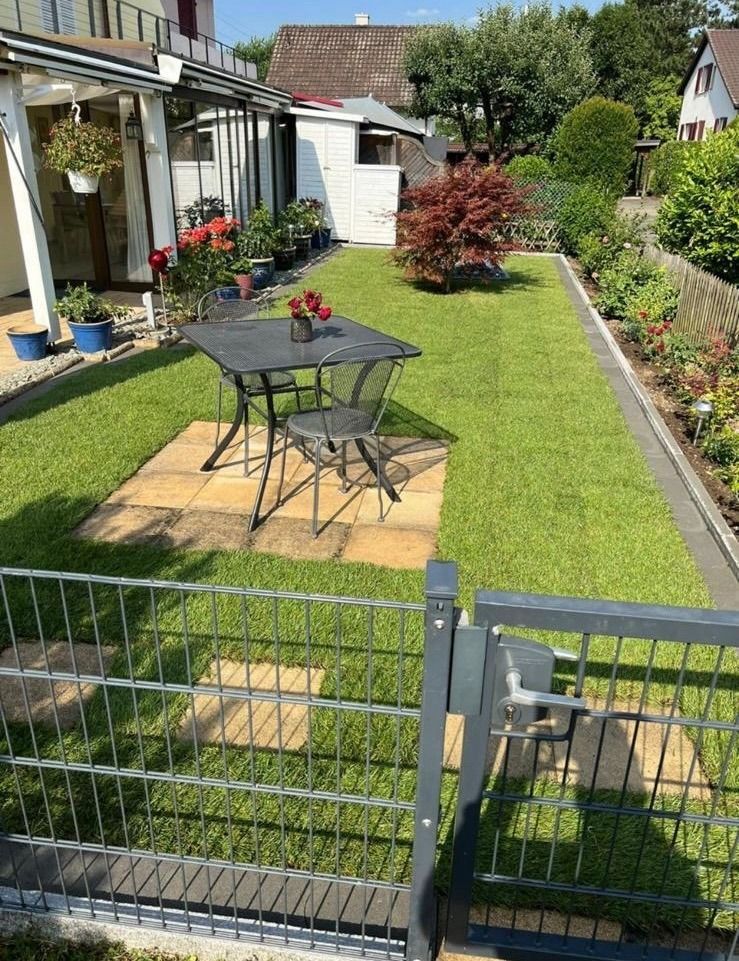 Ein Zaun umgibt einen üppigen grünen Hof mit einem Tisch und Stühlen.